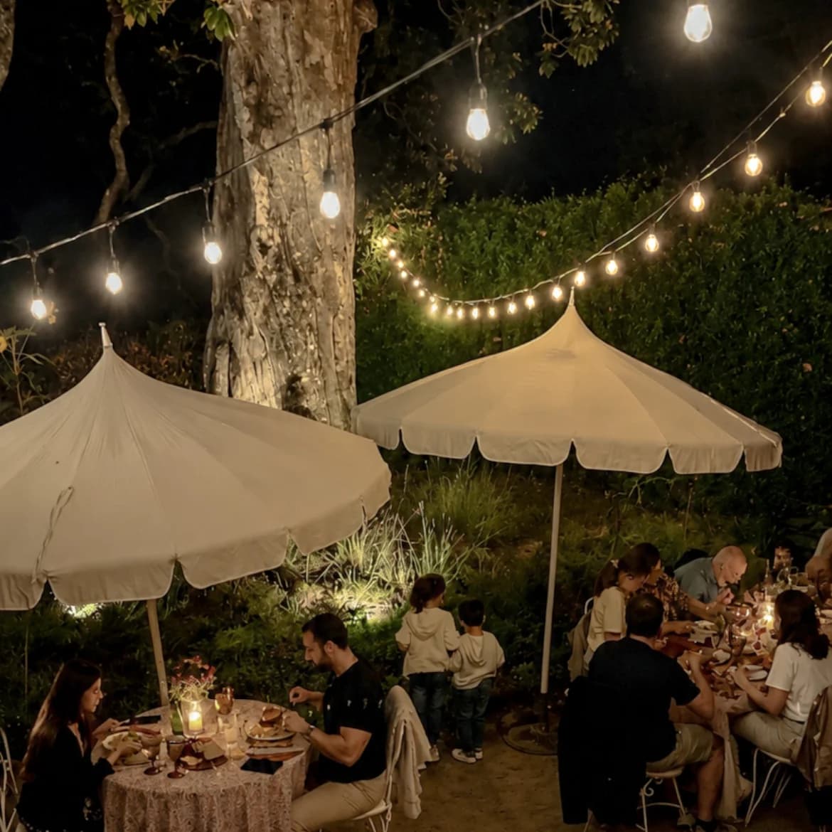 Um jantar no jardim sob guarda-sóis e luzes ao entardecer