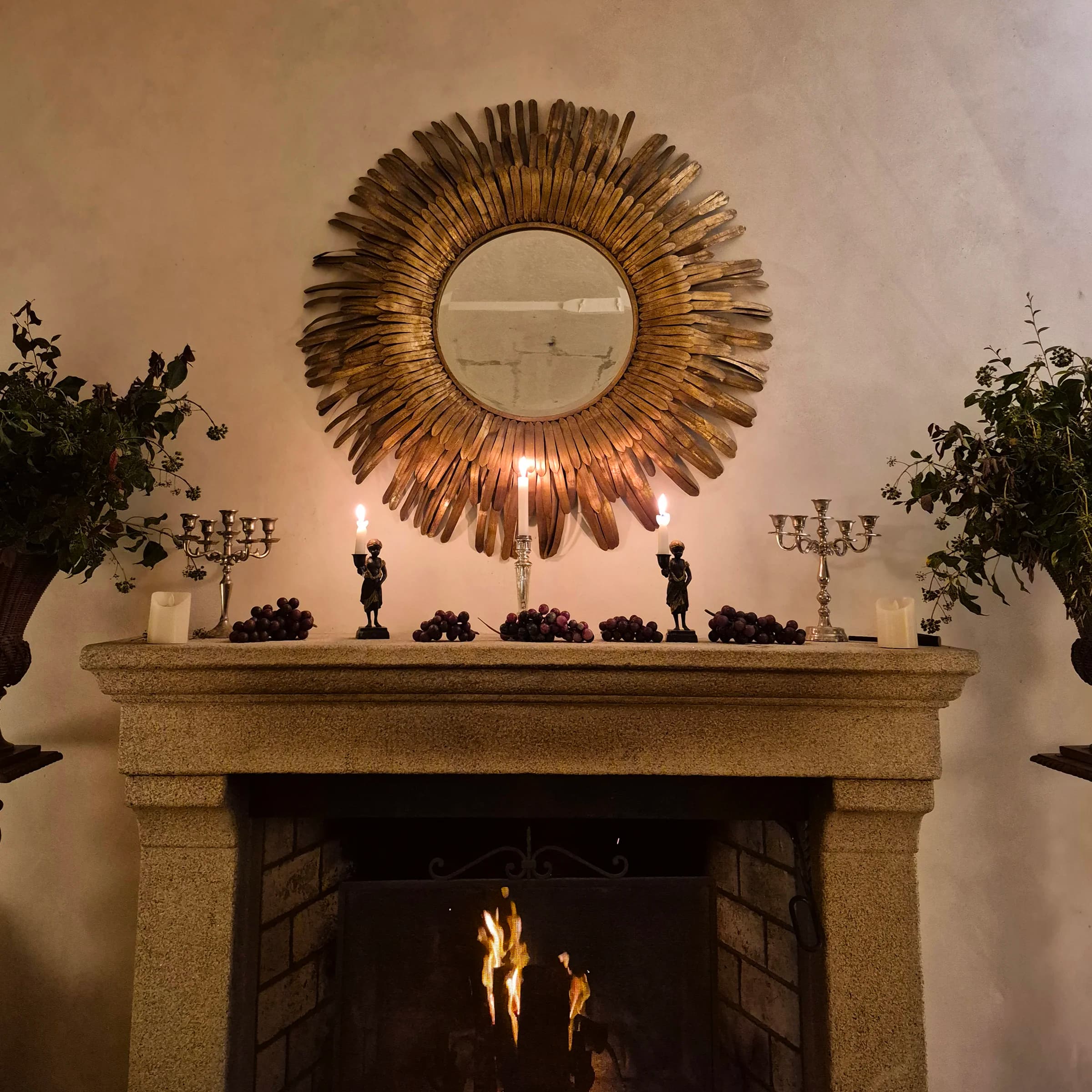 A lareira de pedra decorada com velas e uvas sob um espelho dourado em sol