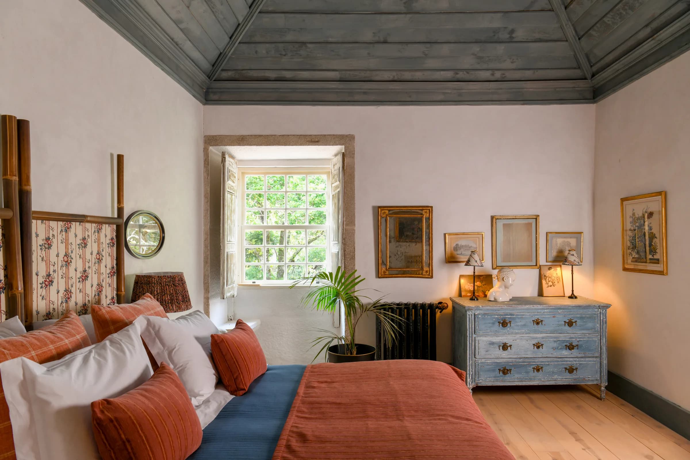 The Lilas suite — the bed beneath the timber ceiling, blue chest of drawers beyond
